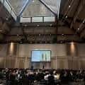 Interior del salón de conferencias con audiencia y pantalla de presentación