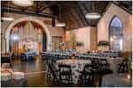 Salón decorado para boda con mesas redondas y arcos blancos bajo techos altos