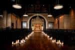 Pasillo central iluminado con velas durante una ceremonia en Clementine Hall