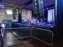 Escenario del venue con equipo de sonido y barreras metálicas en primer plano