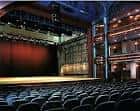 Escenario vacío con telón rojo y platea vacía bajo iluminación dramática