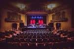 Interior del auditorio del Aladdin Theater con escenario iluminado y butacas vacías