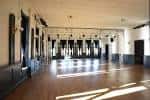 Gran salón vacío con piso de madera y luz natural entrando por ventanas laterales