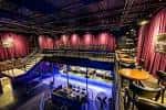 Espacio interior del Summit Music Hall con cortinas rojas, mesas de bar y zona de escenario vacía