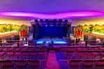 Interior del auditorio con escenario iluminado y butacas rojas dispuestas para eventos