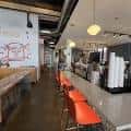 Interior del restaurante con barra de cocina abierta y sillas naranjas