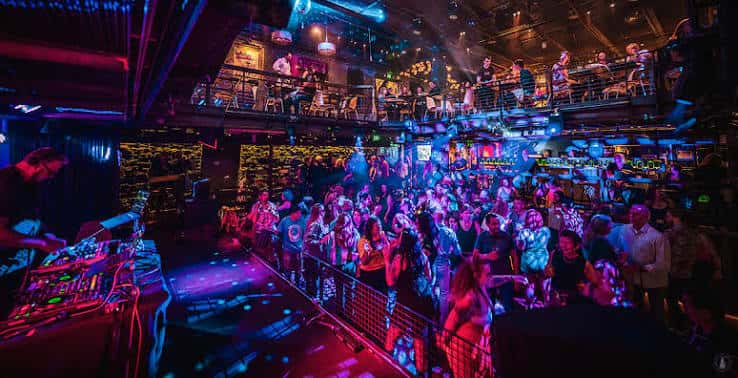 Interior del club con público disfrutando de un evento nocturno y luces de colores