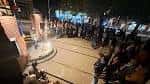 Evento nocturno en la plaza con público reunido alrededor de una fuente iluminada