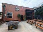 Patio exterior de Crank Arm Brewing Company con mesas de picnic y fogata