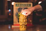 Detalle de una bebida servida en vaso tiki con logo del lugar