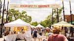 Feria al aire libre con carpas blancas y gente caminando por la calle