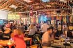 Interior del bar con ambiente festivo, techos altos y clientes disfrutando bebidas