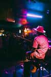 Músico tocando el piano en Slim's Dive Bar con iluminación de neón