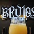 Detalle del logo iluminado de Brujos Brewing sobre una cerveza servida