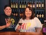 Dos mujeres sonrientes sosteniendo copas de vino en la barra del Hip Chicks Do Wine