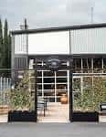 Fachada exterior del establecimiento Westward Whiskey con entrada de cristal y decoración vegetal