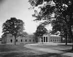 Fotografía histórica en blanco y negro de la fachada principal de la biblioteca rodeada de árboles