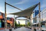 Plaza exterior diurna con toldo geométrico y arquitectura moderna