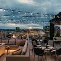 Ambiente nocturno del rooftop con mesas, sofás y vistas a la ciudad