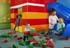 Niños jugando con bloques LEGO y deslizándose por un tobogán azul en zona infantil