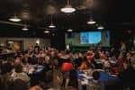 Sala principal del venue con pantalla proyectada y público asistiendo a una presentación o cena