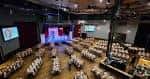 Interior del salón principal con mesas redondas dispuestas para evento y escenario iluminado