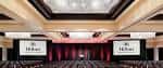 Gran salón de eventos con escenario, pantallas y cortinas rojas