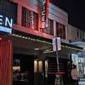 Fachada exterior de The Office Bar por la noche con letrero luminoso