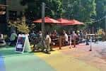 Vista del Rainbow Road Plaza con mesas y sombrillas rojas en un ambiente al aire libre
