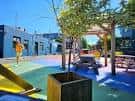 Área recreativa del plaza con árboles, bancos y estructuras modernas bajo cielo despejado