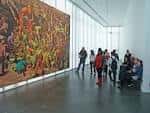 Interior del museo con visitantes observando una gran obra de arte en la pared