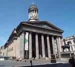 Vista exterior del edificio de la Galería de Arte Moderno (GoMA) en Glasgow con fachada neoclásica y columnas bajo cielo azul
