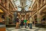 Salón central con esqueleto de dinosaurio suspendido y grupo de personas observando la exhibición
