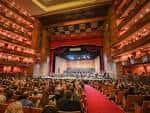 Interior del auditorio principal con butacas rojas, escenario iluminado y decoración clásica