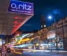 Vista nocturna del exterior del O2 Ritz Manchester con el letrero iluminado y luces de tráfico en movimiento