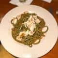 Plato de pasta verde con mariscos servido en plato blanco