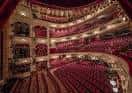 Interior del auditorio con butacas rojas, balcones ornamentados y escenario iluminado