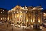 Vista nocturna del exterior del teatro con iluminación cálida y ambiente elegante