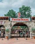 Entrada principal de Six Flags Fiesta Texas con letrero y arcos de piedra
