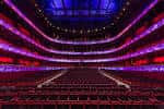 Interior del auditorio con butacas rojas y escenario bajo luces de colores