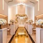 Ceremonia de boda en un espacio blanco con pasillo dorado y arreglos florales