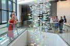 Instalación artística interior con figuras colgantes y visitantes observando