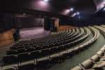 Interior del auditorio principal con butacas dispuestas en gradas y escenario iluminado