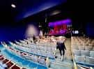 Escenario con luces de colores y gradas azules en disposición para evento