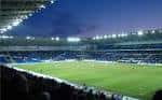 Vista nocturna del interior del Cardiff City Stadium con el campo de juego iluminado y gradas llenas