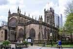 Fachada lateral de la Catedral de Manchester con detalles arquitectónicos góticos y personas caminando en los jardines