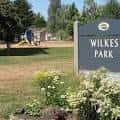 Señal de entrada del Wilkes Park con jardín y área verde al fondo