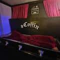 Interior del Coffin Club con un ataúd decorativo y cortinas rojas