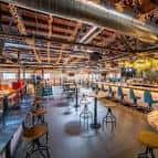 Salón principal con barra, mesas altas y decoración industrial