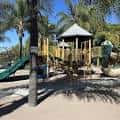 Área de juegos infantil con tobogán y estructura de madera bajo palmeras